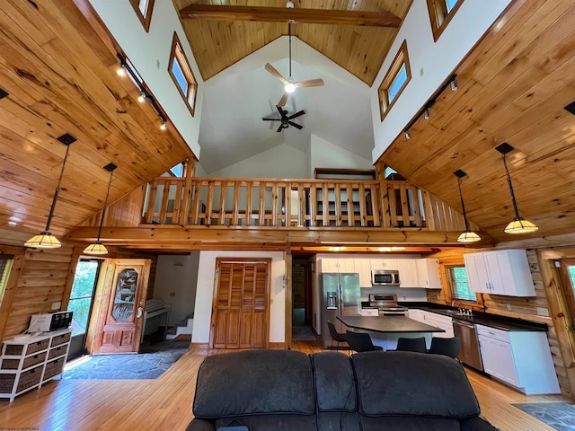 living room with ceiling fan, wood walls, light wood-type flooring, and high vaulted ceiling