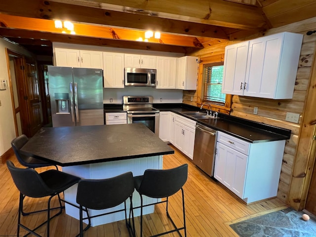 kitchen featuring sink, light hardwood / wood-style flooring, appliances with stainless steel finishes, beam ceiling, and white cabinetry