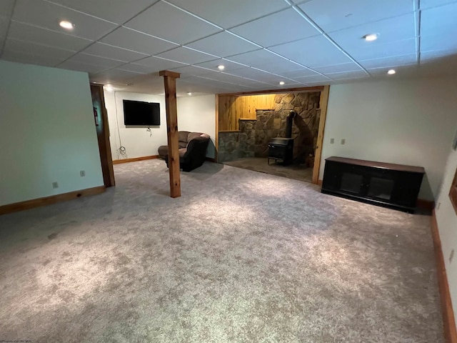 basement featuring carpet flooring, a wood stove, and a drop ceiling