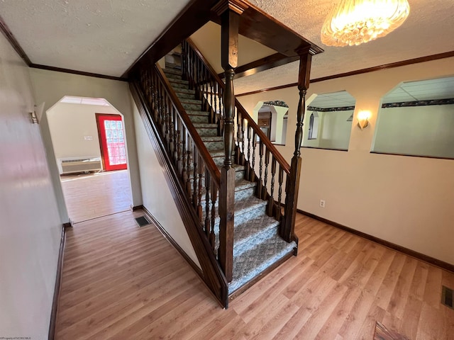 staircase with wood-type flooring, a textured ceiling, an inviting chandelier, and crown molding