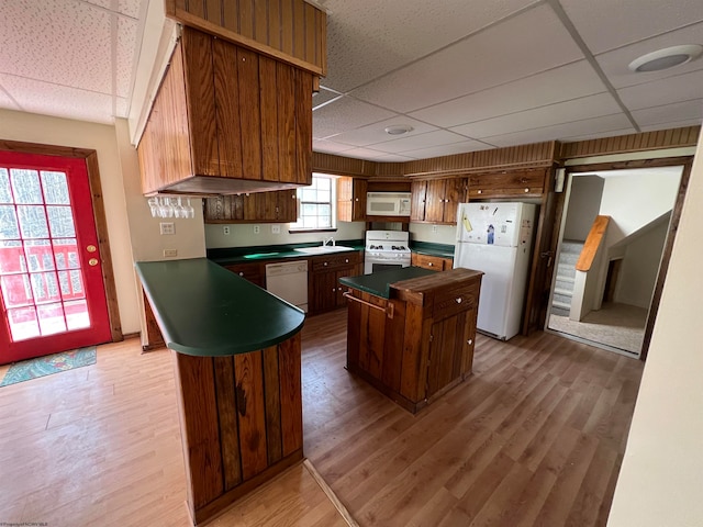 kitchen with a paneled ceiling, a kitchen island, wood-type flooring, and white appliances