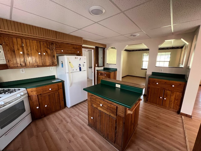 kitchen with a paneled ceiling, wood walls, white appliances, a kitchen island, and light hardwood / wood-style floors