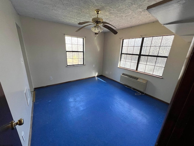 empty room with ceiling fan, a healthy amount of sunlight, an AC wall unit, and a textured ceiling