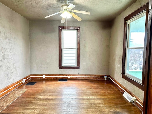 empty room with ceiling fan, wood-type flooring, and a textured ceiling