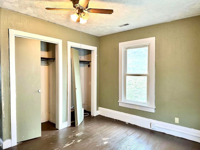 unfurnished bedroom with ceiling fan, dark wood-type flooring, and two closets