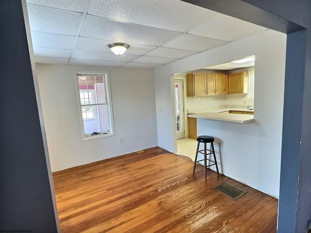 kitchen with kitchen peninsula, a breakfast bar, hardwood / wood-style floors, and a drop ceiling