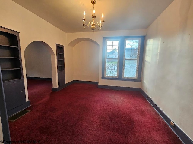 carpeted spare room featuring built in features and an inviting chandelier