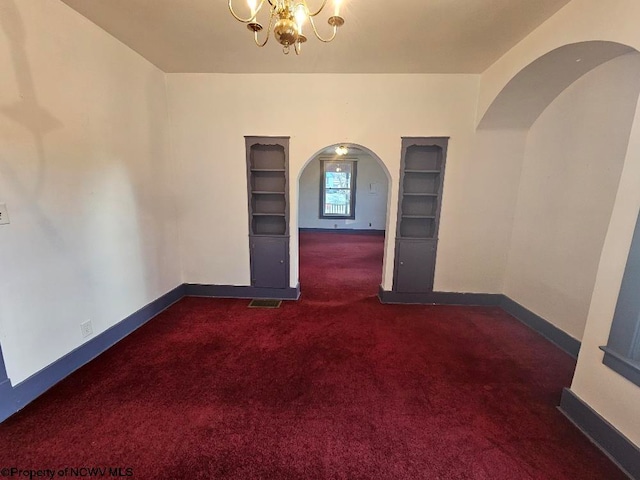 spare room featuring dark colored carpet, built in features, and a notable chandelier