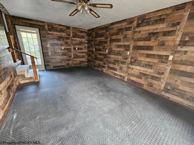 unfurnished room featuring ceiling fan, wood walls, and a textured ceiling