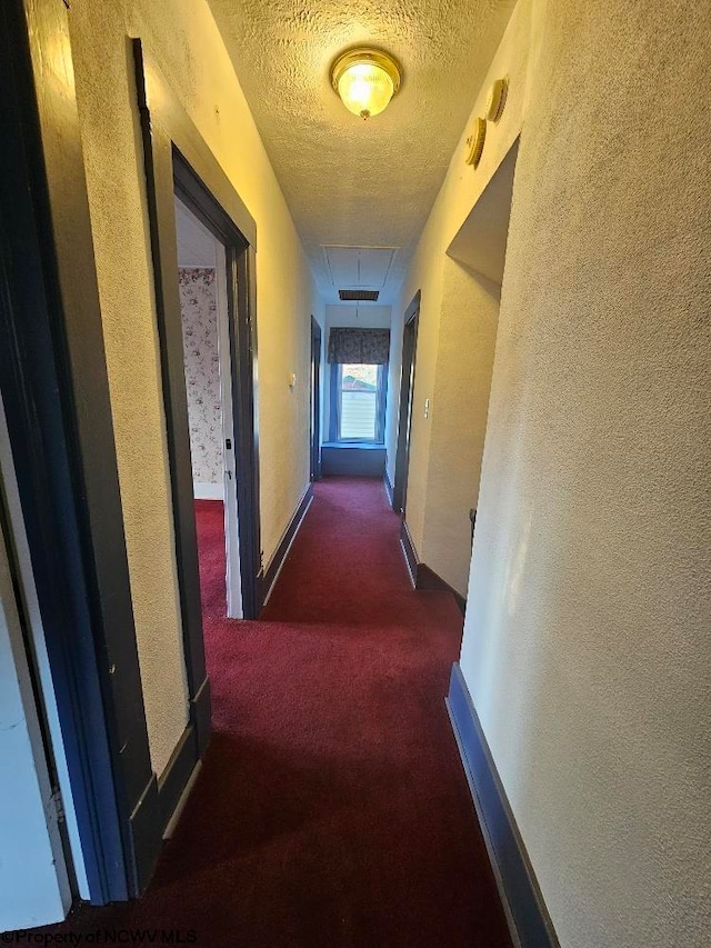 corridor featuring dark carpet and a textured ceiling