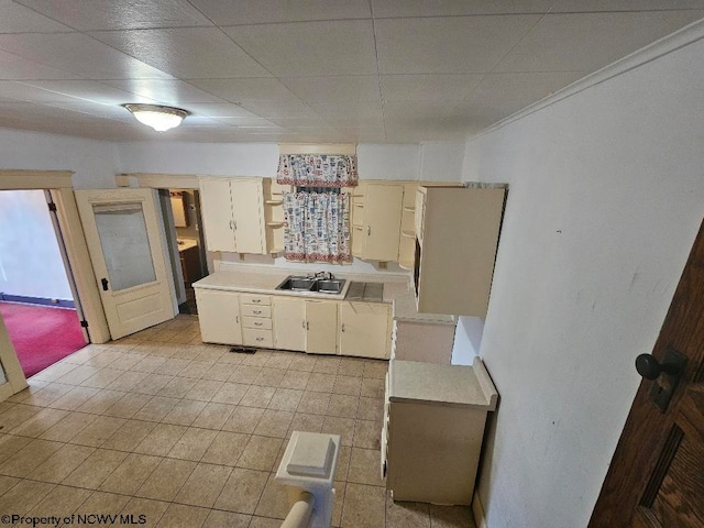 kitchen with cream cabinets, light tile patterned floors, crown molding, and sink