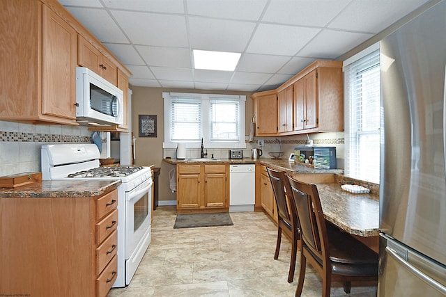 kitchen featuring a paneled ceiling, decorative backsplash, sink, and white appliances