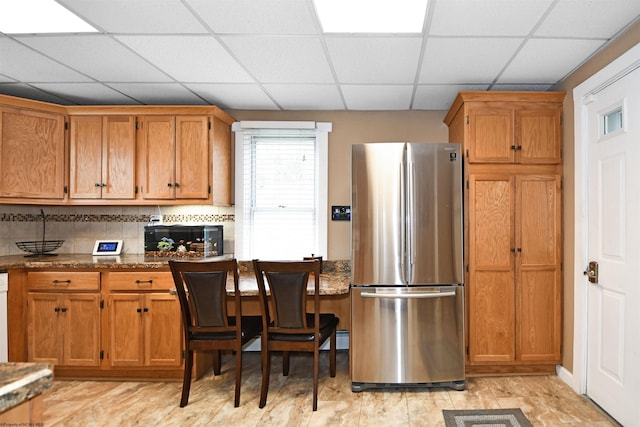 kitchen with stainless steel fridge, backsplash, a drop ceiling, and dark stone countertops