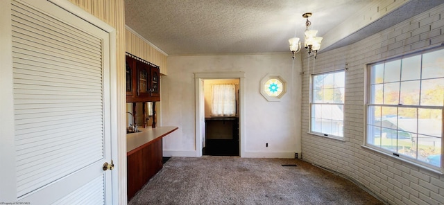 unfurnished dining area featuring crown molding, a textured ceiling, a notable chandelier, carpet floors, and brick wall