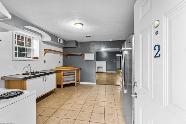 kitchen featuring stainless steel refrigerator, white cabinetry, sink, and light tile patterned floors