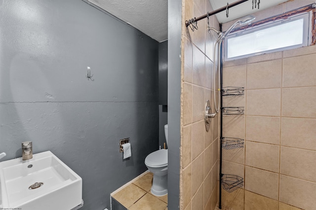 bathroom featuring a tile shower, sink, tile patterned flooring, a textured ceiling, and toilet