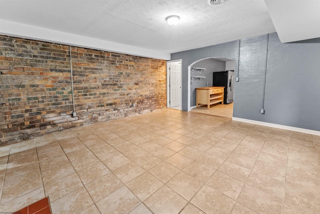 tiled spare room with a textured ceiling and brick wall