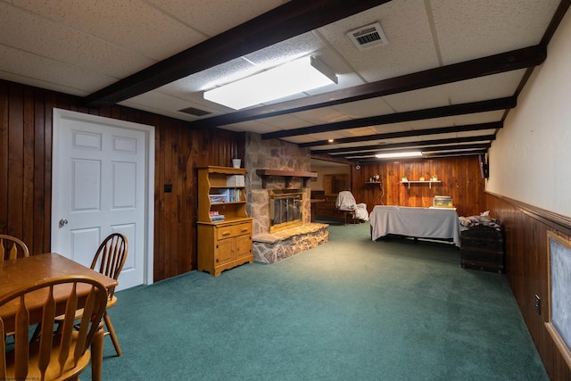 carpeted bedroom with beam ceiling, a stone fireplace, and wood walls