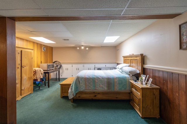 carpeted bedroom featuring a paneled ceiling and wood walls