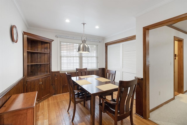 dining room featuring light wood-type flooring, ornamental molding, and wooden walls