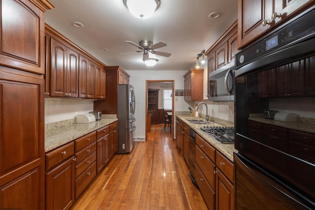 kitchen featuring appliances with stainless steel finishes, light stone counters, ceiling fan, sink, and light hardwood / wood-style floors