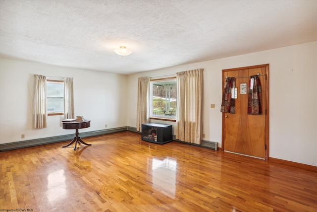 empty room featuring wood-type flooring, a textured ceiling, and a baseboard heating unit