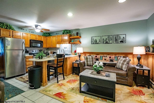 kitchen featuring a kitchen bar, appliances with stainless steel finishes, decorative backsplash, ceiling fan, and light tile patterned floors