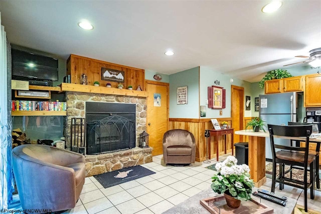 living room featuring ceiling fan, a fireplace, light tile patterned flooring, and wood walls