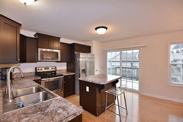 kitchen with a kitchen breakfast bar, light wood-type flooring, stainless steel appliances, sink, and a center island