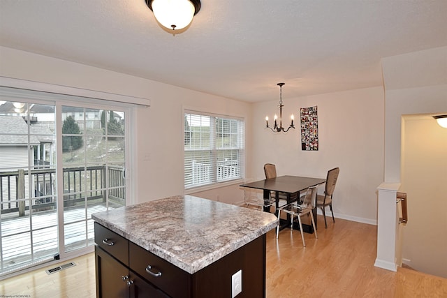 kitchen featuring light wood-type flooring, dark brown cabinets, pendant lighting, a notable chandelier, and a center island