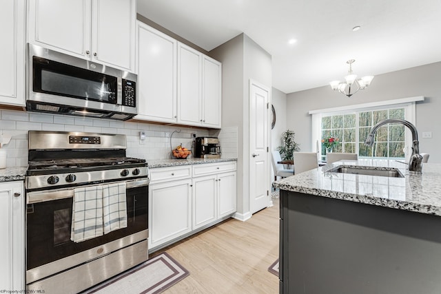 kitchen with sink, stainless steel appliances, a notable chandelier, white cabinets, and light wood-type flooring