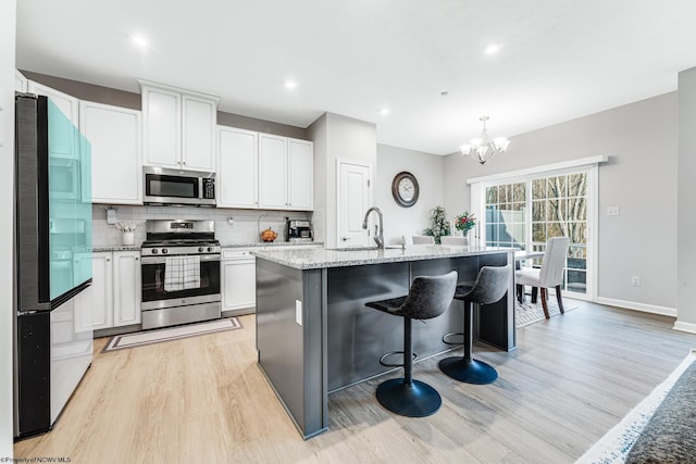 kitchen featuring white cabinetry, stainless steel appliances, backsplash, an island with sink, and light wood-type flooring