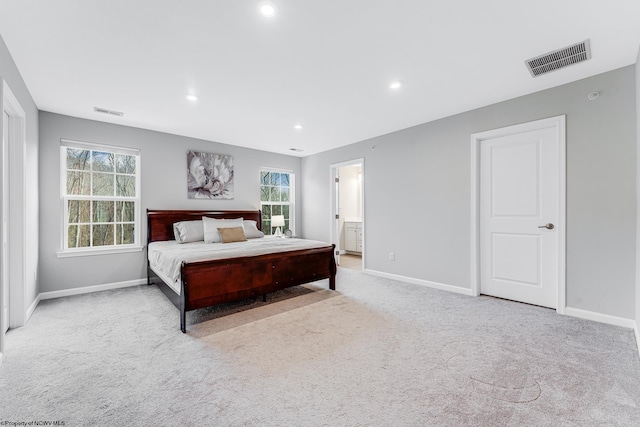 carpeted bedroom with ensuite bathroom and multiple windows