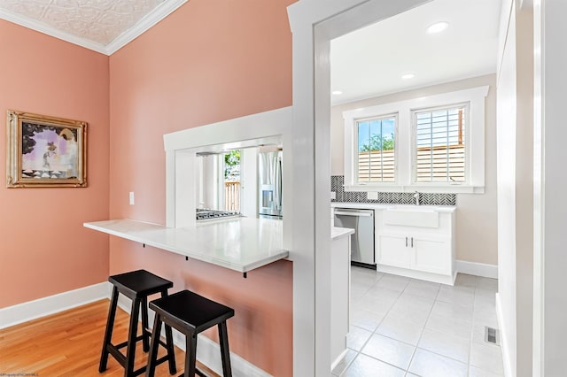 kitchen with white cabinets, ornamental molding, appliances with stainless steel finishes, a kitchen bar, and kitchen peninsula