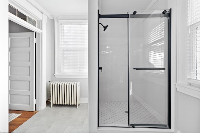 bathroom featuring a shower with shower door, wood-type flooring, ornamental molding, and radiator