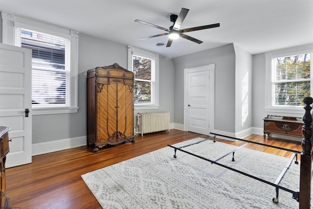 bedroom with ceiling fan, radiator heating unit, dark wood-type flooring, and multiple windows