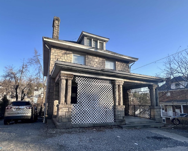 american foursquare style home featuring stone siding, a porch, and a chimney