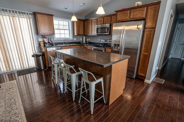 kitchen with dark wood-type flooring, decorative light fixtures, vaulted ceiling, a kitchen island, and appliances with stainless steel finishes