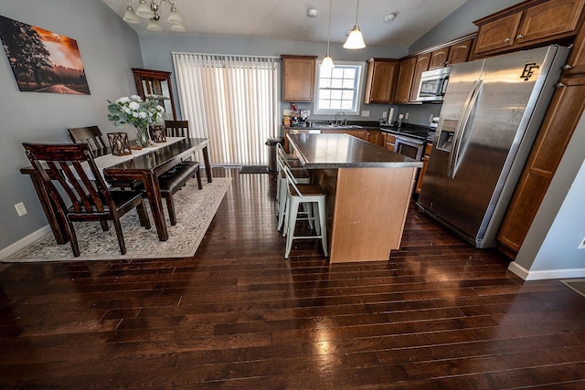 kitchen featuring stainless steel appliances, vaulted ceiling, dark wood-type flooring, a center island, and hanging light fixtures