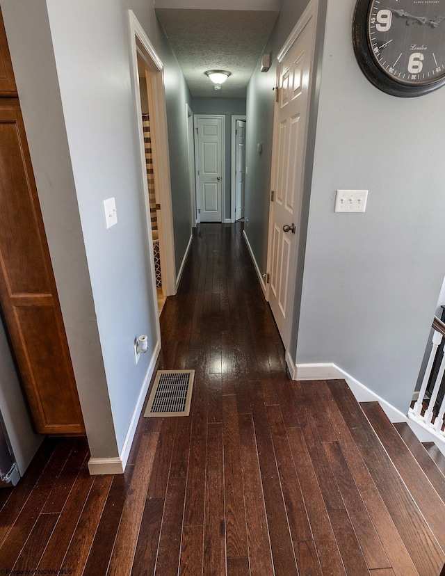 hall with a textured ceiling and dark wood-type flooring