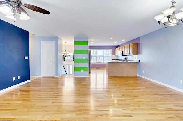 kitchen with ceiling fan with notable chandelier, light wood-type flooring, tasteful backsplash, kitchen peninsula, and stainless steel appliances