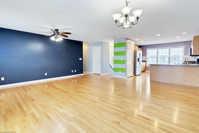 unfurnished living room with ceiling fan with notable chandelier, light hardwood / wood-style floors, and sink