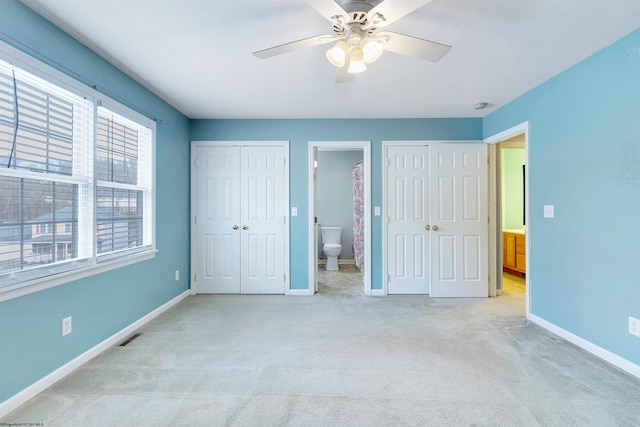 unfurnished bedroom with multiple closets, ensuite bathroom, ceiling fan, and light colored carpet