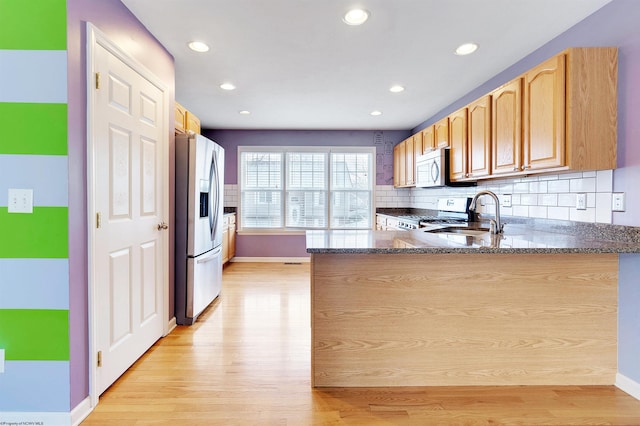 kitchen featuring kitchen peninsula, decorative backsplash, dark stone counters, stainless steel appliances, and light hardwood / wood-style flooring