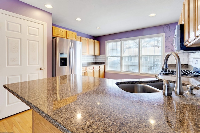 kitchen featuring stainless steel refrigerator with ice dispenser, light wood-type flooring, tasteful backsplash, dark stone counters, and sink