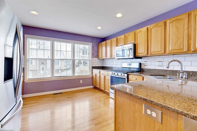 kitchen featuring sink, tasteful backsplash, light stone counters, light hardwood / wood-style flooring, and appliances with stainless steel finishes