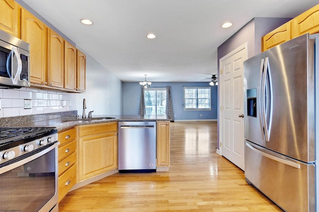 kitchen with appliances with stainless steel finishes, ceiling fan with notable chandelier, light hardwood / wood-style flooring, and sink