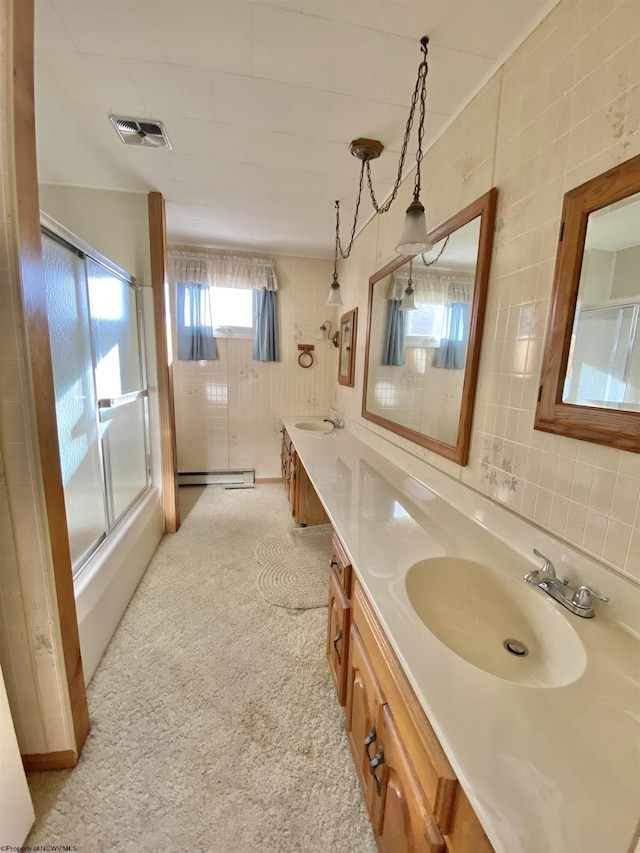 bathroom with baseboard heating, shower / bath combination with glass door, vanity, and tile walls