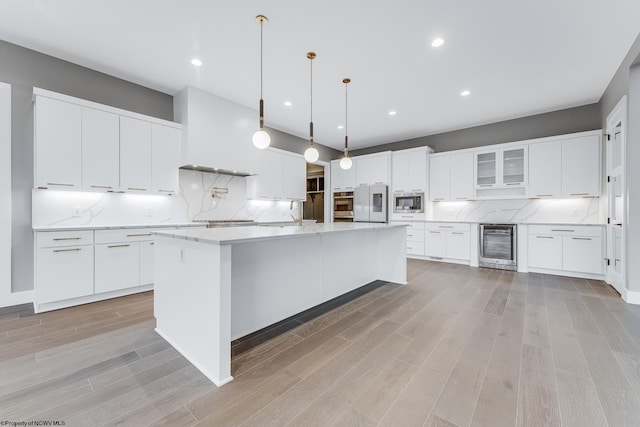 kitchen featuring glass insert cabinets, beverage cooler, white cabinets, an island with sink, and decorative light fixtures