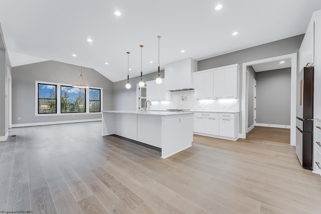 kitchen featuring an island with sink, custom range hood, light wood-type flooring, white cabinetry, and pendant lighting